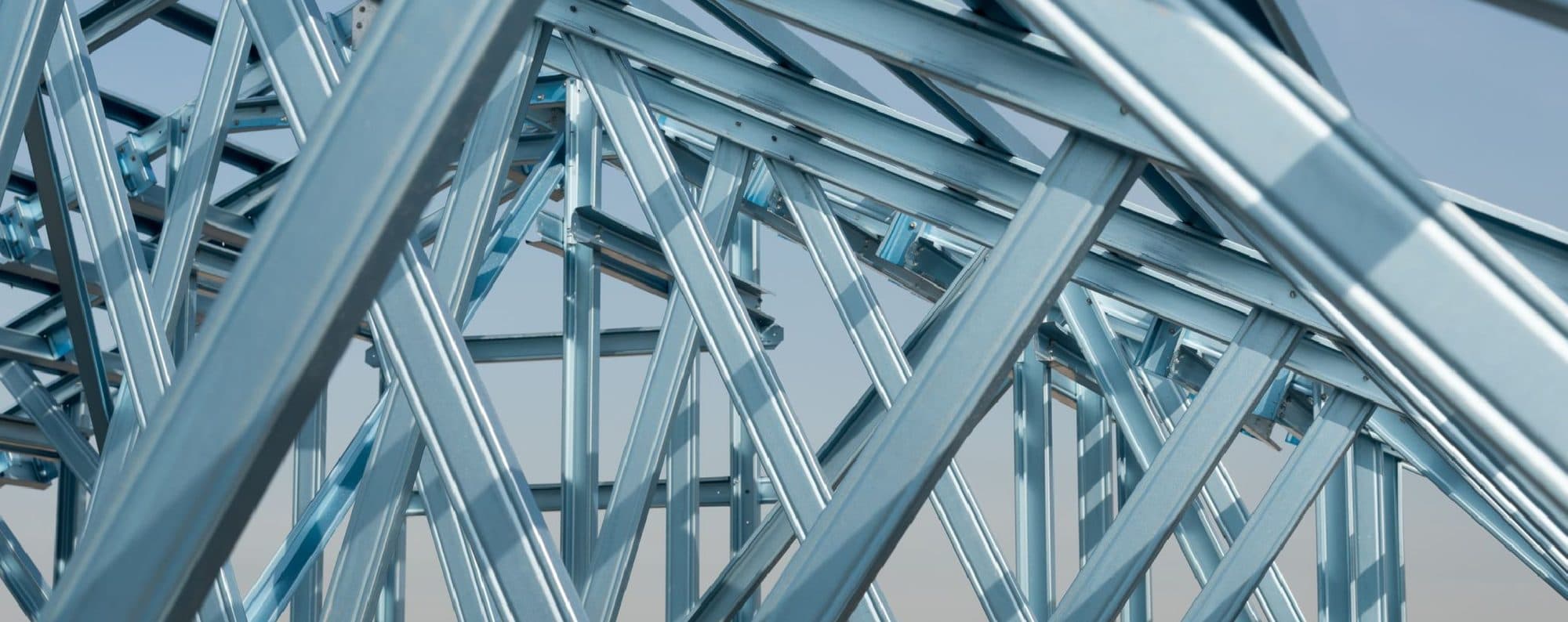 Galvanised steel roof trusses against a pale sky